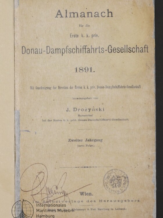 Vergilbtes Titelblatt eines Almanachs der Ersten k. k. priv. Donau-Dampfschiffahrts-Gesellschaft von 1891 mit gedrucktem Titel und Herausgeberangabe J. Drożyński, handschriftlicher Unterschrift, runden Stempelabdrucken und Museum-Logo unten links.