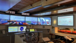Schiffsbrücken-Simulator mit Steuerrad, mehreren Bildschirmen mit Containerhafenansichten und Rettungsring 'PT EXPRESS'.