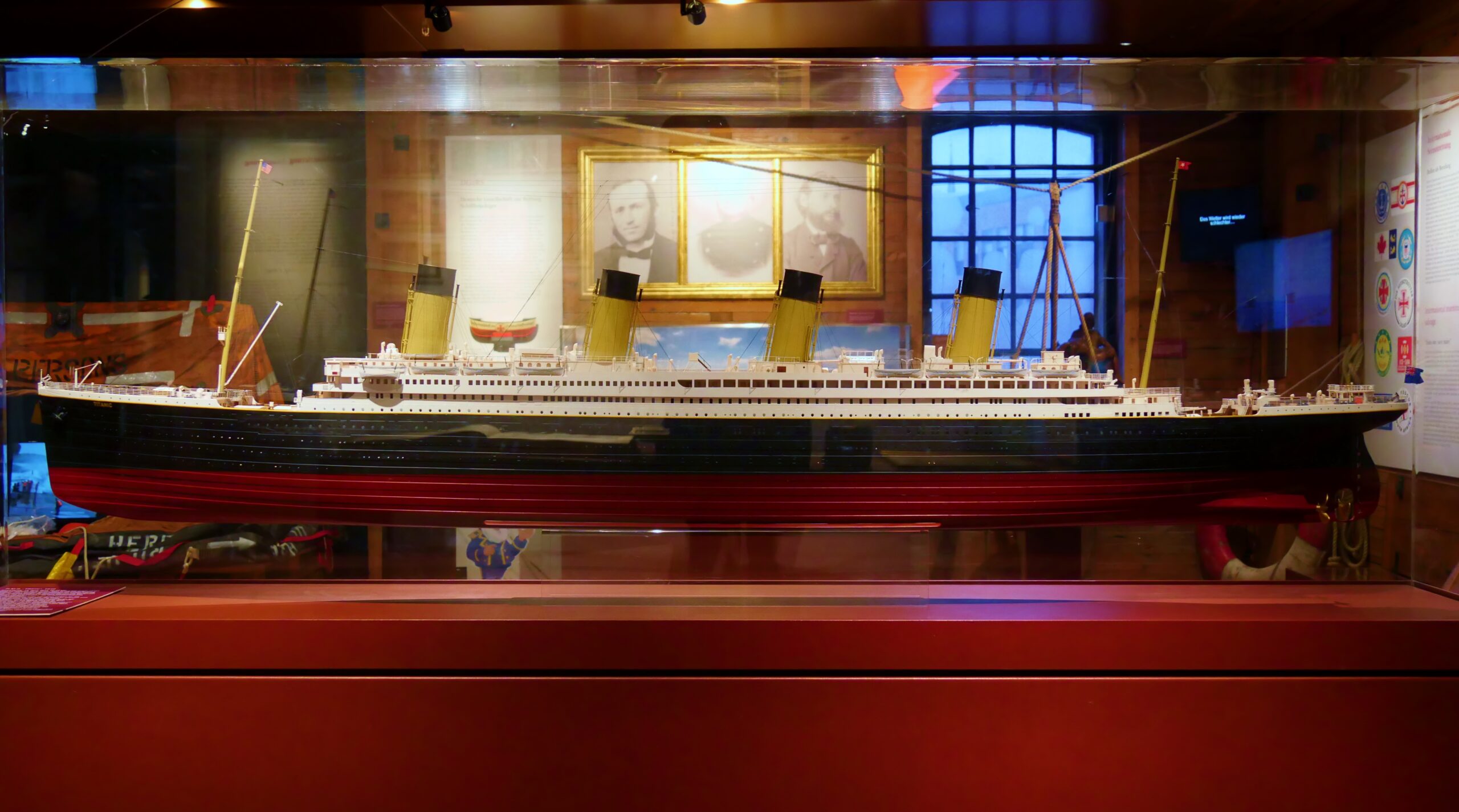 Modellschiff eines großen Ozeandampfers mit vier gelben Schornsteinen und schwarzem Rumpf mit rotem Kiel in einer Glasvitrine.
