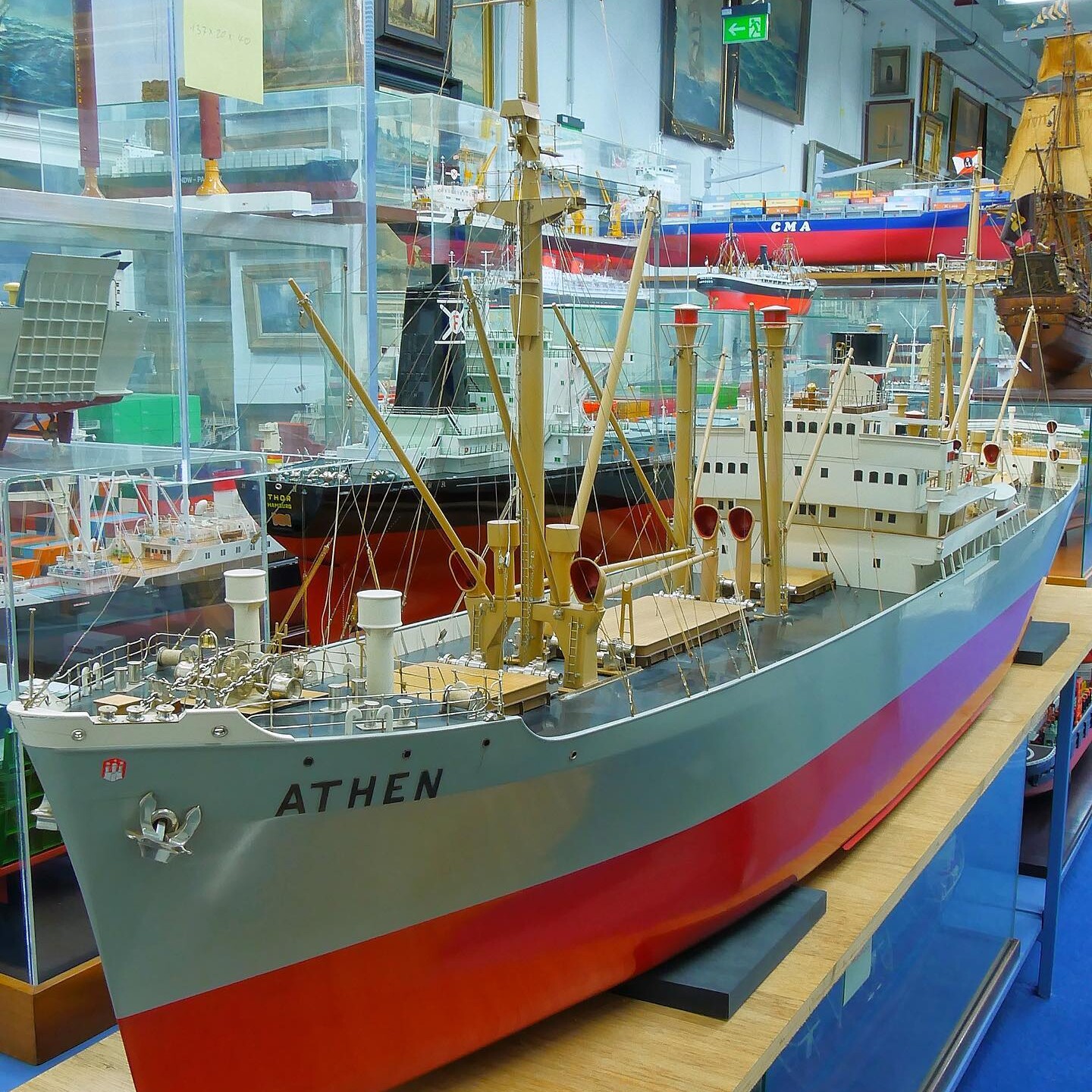 Großes Modellschiff mit Namen ATHEN in Museumsvitrine, sichtbare Masten, Decksaufbauten und rote Wasserlinie.
