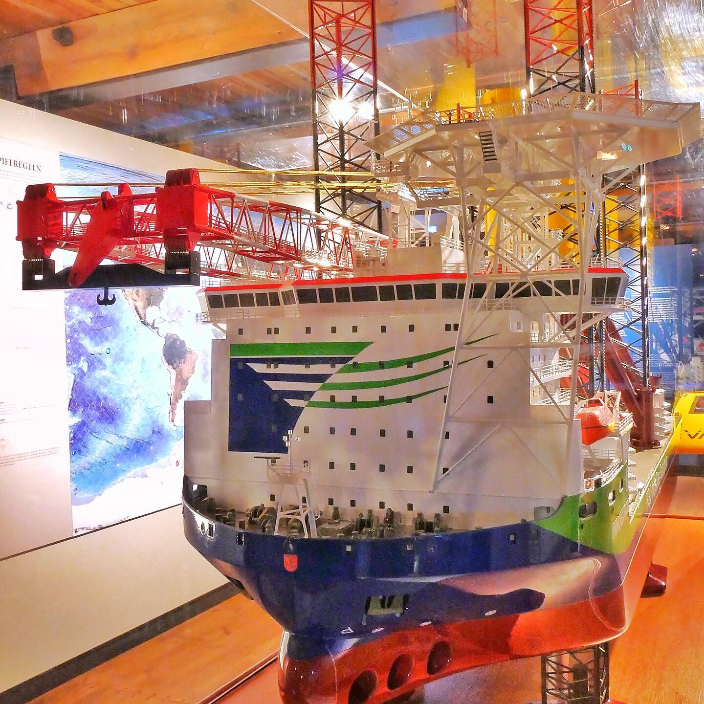 Modell eines großen Offshore-Schiffs mit rotem Kranarm, hellen Decksstrukturen und markanten Stützen im Ausstellungsraum