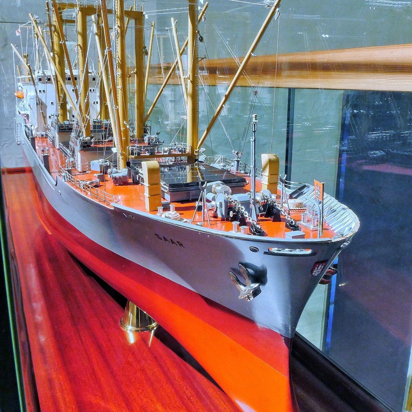 Detailliertes Schiffsmodell mit roten Decks, gelben Masten und komplexem Takelwerk auf glänzendem Holzsockel.