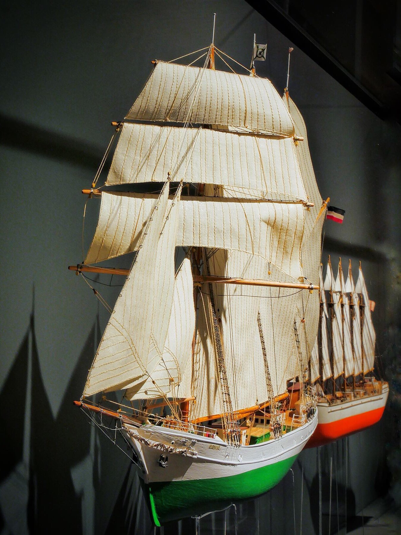 Detailliertes Modell eines Segelschiffs mit weiß-beigen Rahsegeln, grüner Bugfarbe und fein gearbeiteter Takelage in Museumsvitrine.