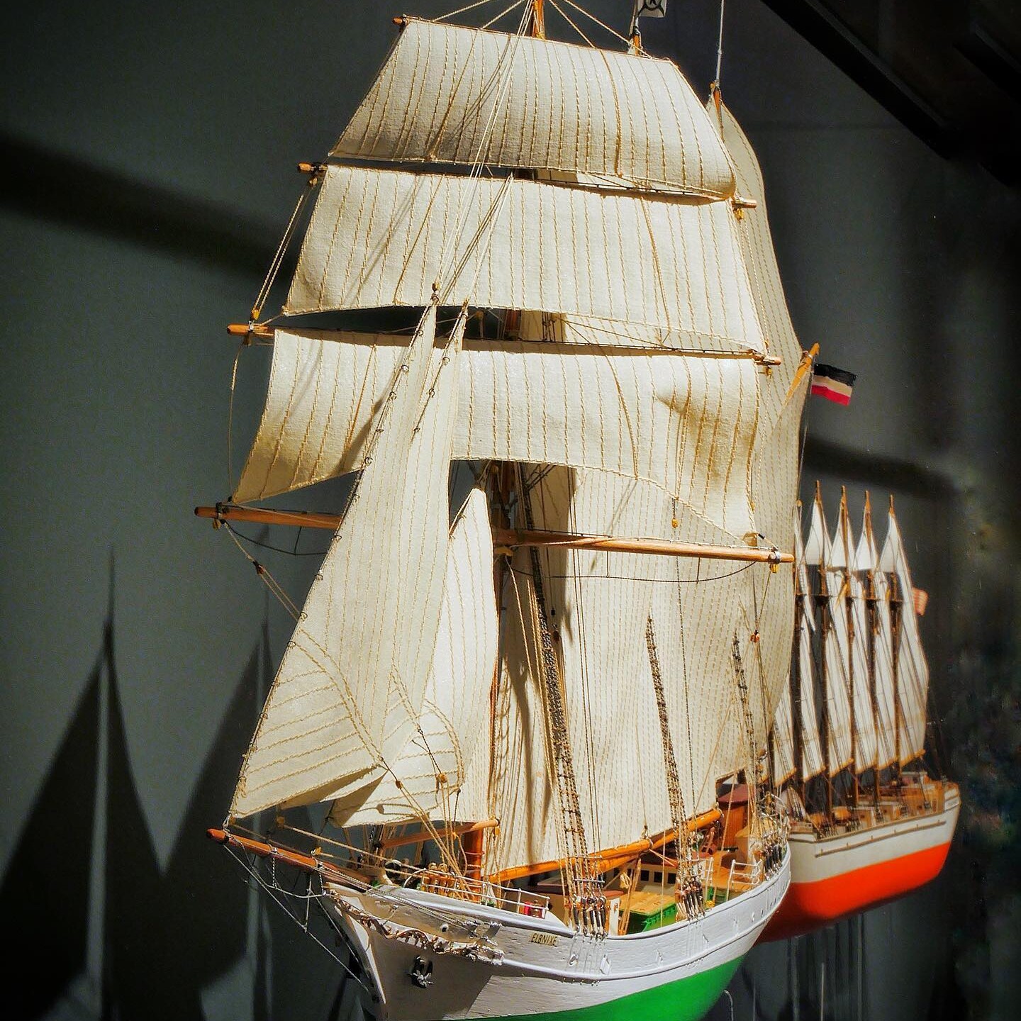 Detailliertes Modell eines Segelschiffs mit weiß-beigen Rahsegeln, grüner Bugfarbe und fein gearbeiteter Takelage in Museumsvitrine.