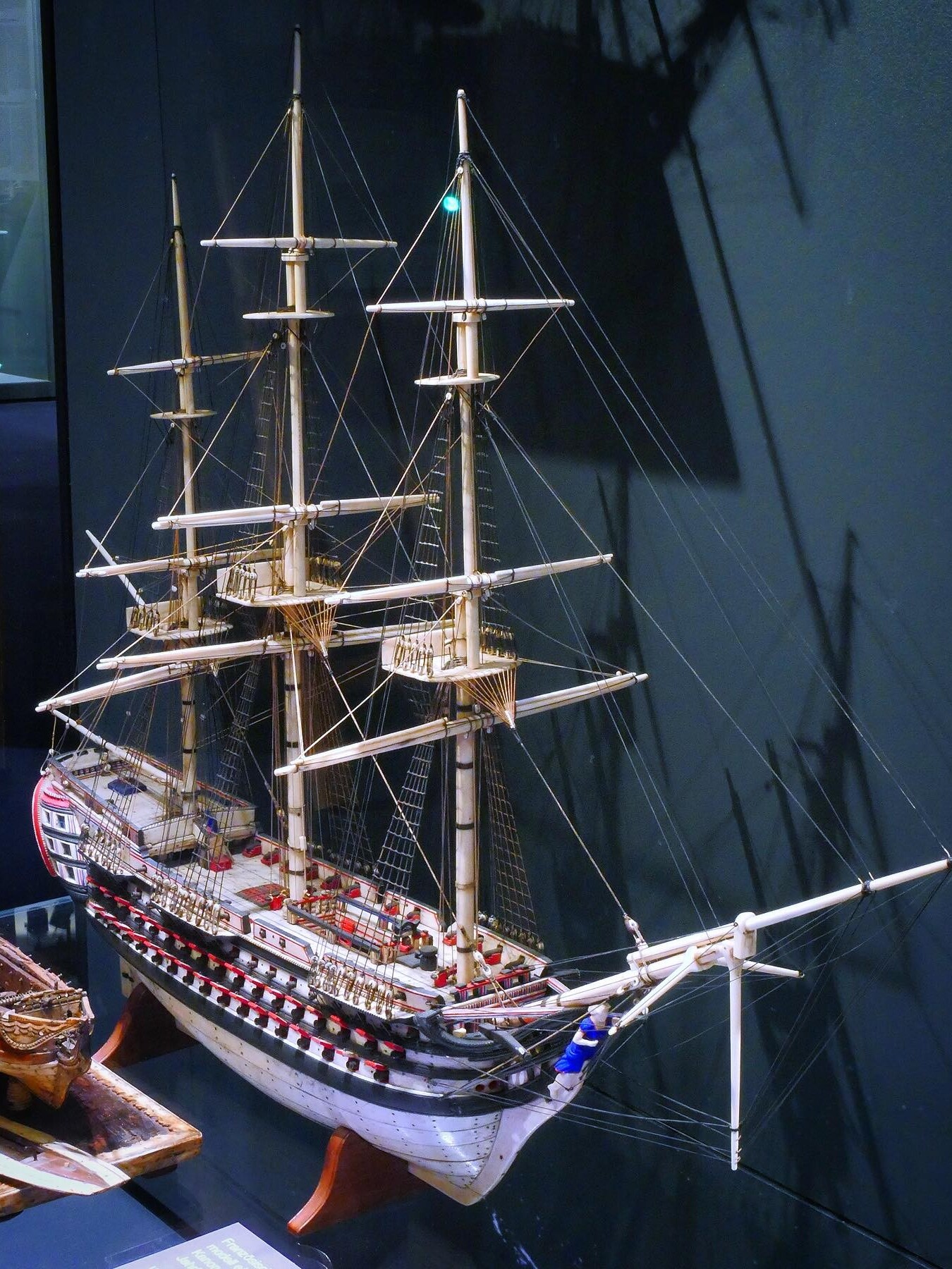Detailliertes Modell eines Dreimast-Seglers mit Takelage, Relingkanonen und bemaltem Rumpf in einer Vitrine.