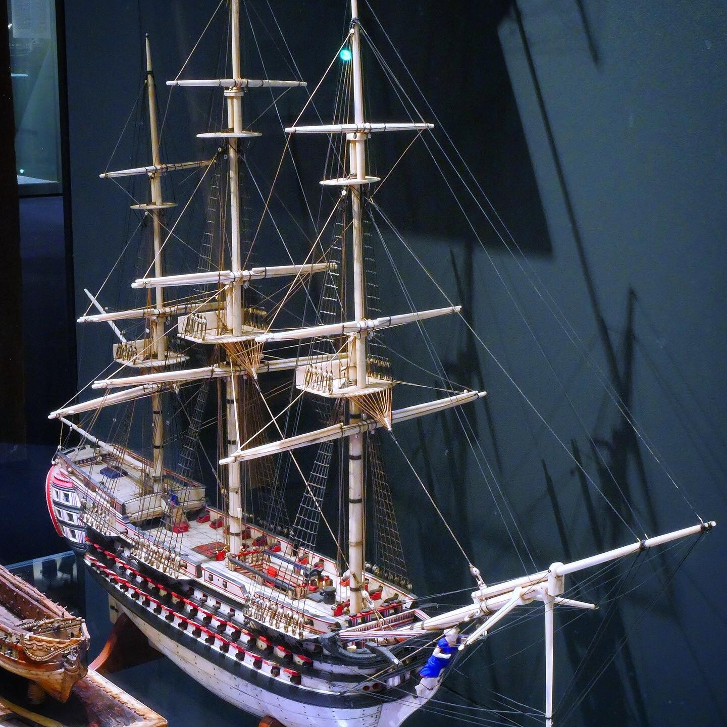 Detailliertes Modell eines Dreimast-Seglers mit Takelage, Relingkanonen und bemaltem Rumpf in einer Vitrine.