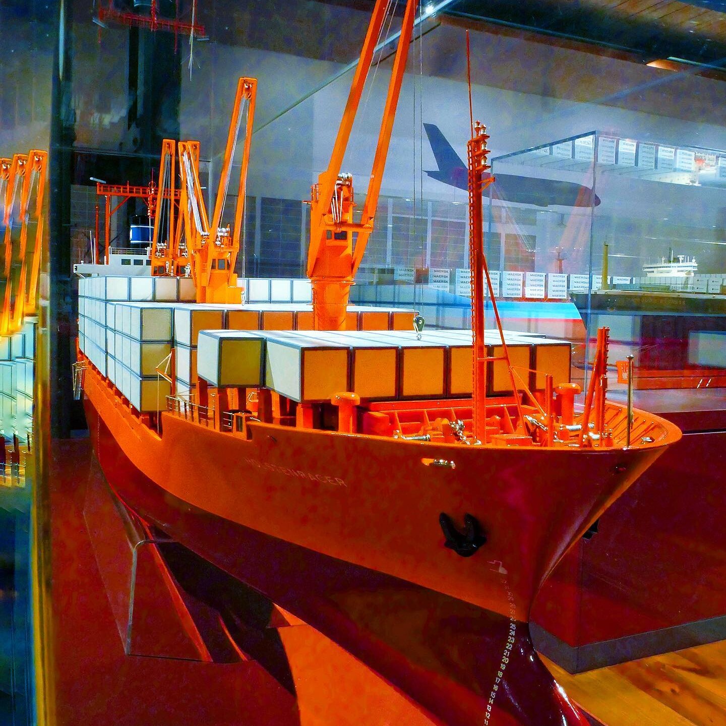 Rotes Containerschiff-Modell in Museumsvitrine mit aufgestapelten Containerblöcken und hohen Ladekränen.
