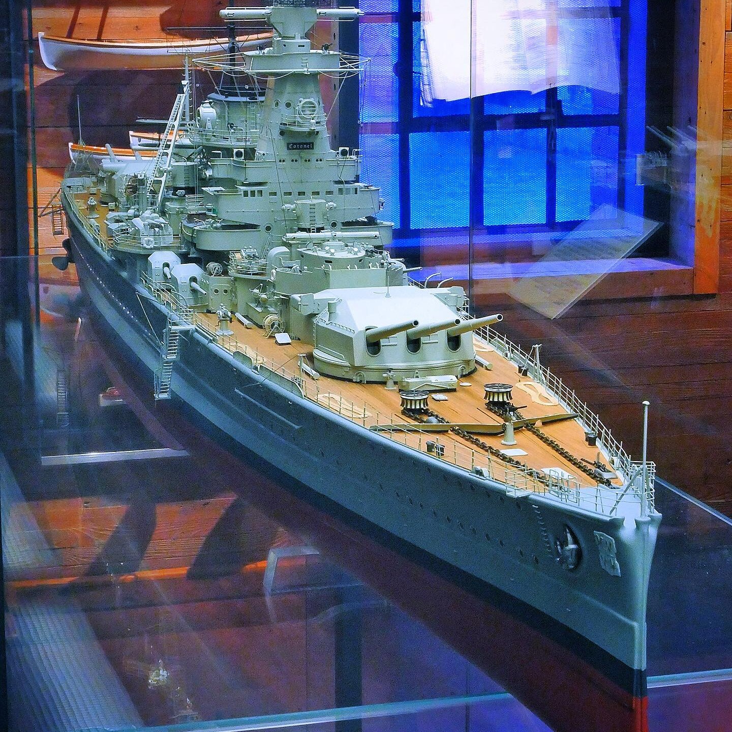 Detailliertes Schiffsmodell eines Schlachtschiffs mit vorderer Dreifachturm-Bewaffnung und sichtbarem Deck in einer Glasvitrine.