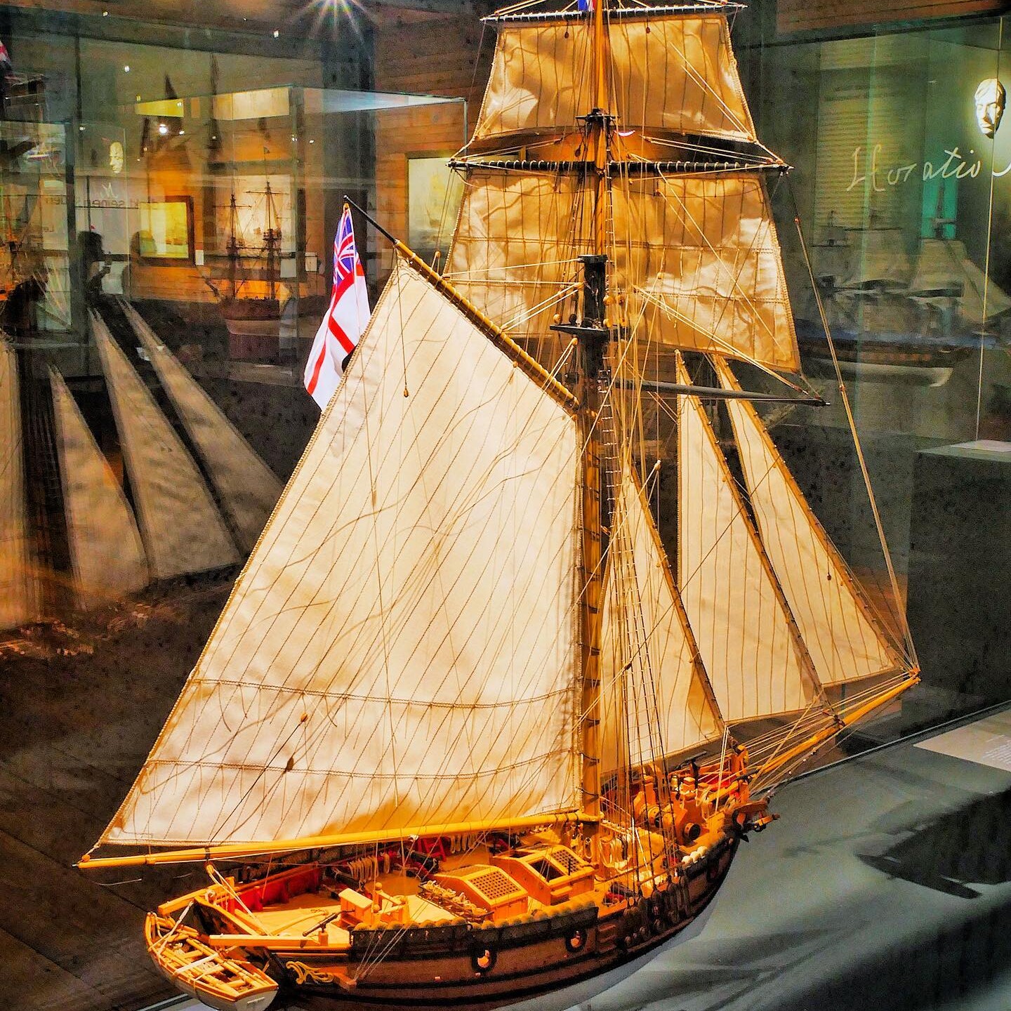 Holzmodell eines historischen Segelschiffs mit aufgeriggten Tuchsegeln, Takelage und britischer Flagge in Museumsvitrine.