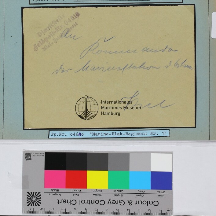 Handschriftlicher gelblicher Briefzettel auf blauem Passepartout mit Museumslogo und Typenschild „Marine‑Flak‑Regiment Nr. 1“, darunter Farb- und Graukeil.
