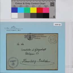 Feldpostumschlag mit handschriftlicher Adresse, NS-Adler-Stempel unten links, Kreisstempel oben rechts und Museumslogo auf hellblauem Hintergrund; Farbkarte oben.