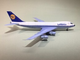 Passagierflugzeug im Lufthansa-Design als Modell mit weißem Rumpf, blauem Heck und vier Triebwerken, seitliche Ansicht auf hellem Hintergrund