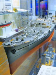 Detailliertes Schiffsmodell in Museumsvitrine mit Decksaufbauten, Kränen, Rettungsbooten und sichtbarem Rumpf in Rot und Schwarz.