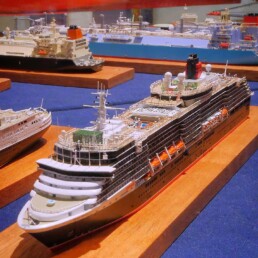 Detailliertes Modell eines großen Kreuzfahrtschiffs mit Deckpools, Rettungsbooten und Schornstein, ausgestellt auf Holzsockel neben weiteren Schiffsmodellen