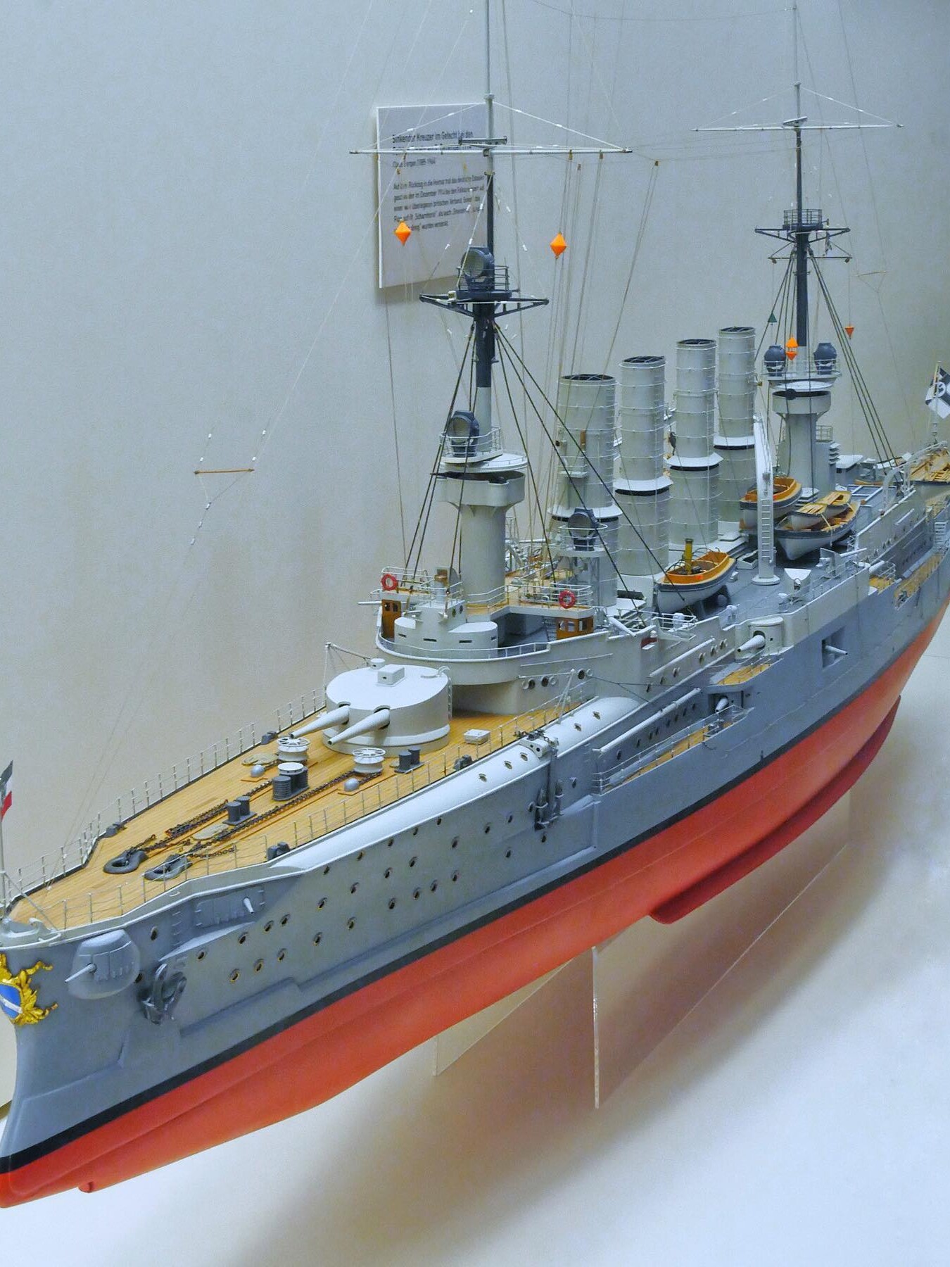 Detailliertes Modell eines historischen Kriegsschiffs mit mehreren Schornsteinen, Masten, Beibooten und hellbraunem Deck.