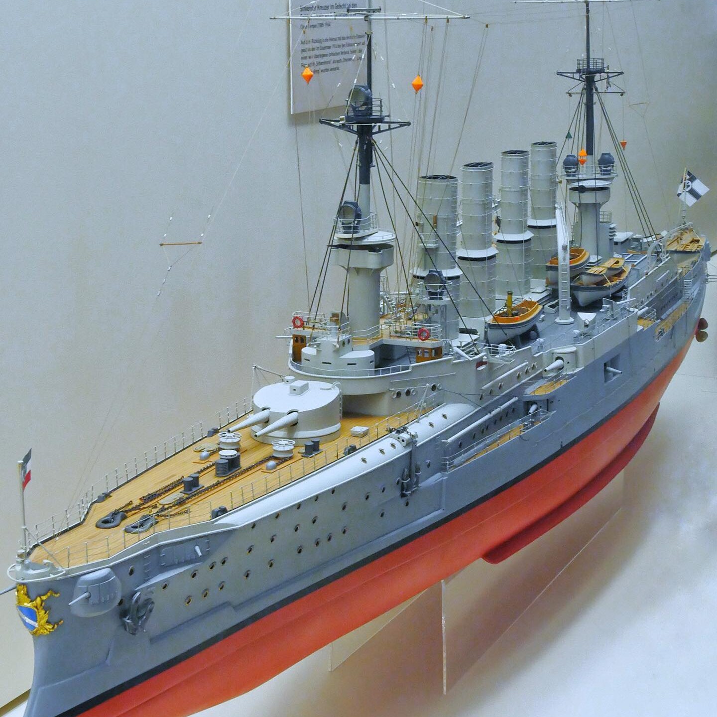Detailliertes Modell eines historischen Kriegsschiffs mit mehreren Schornsteinen, Masten, Beibooten und hellbraunem Deck.