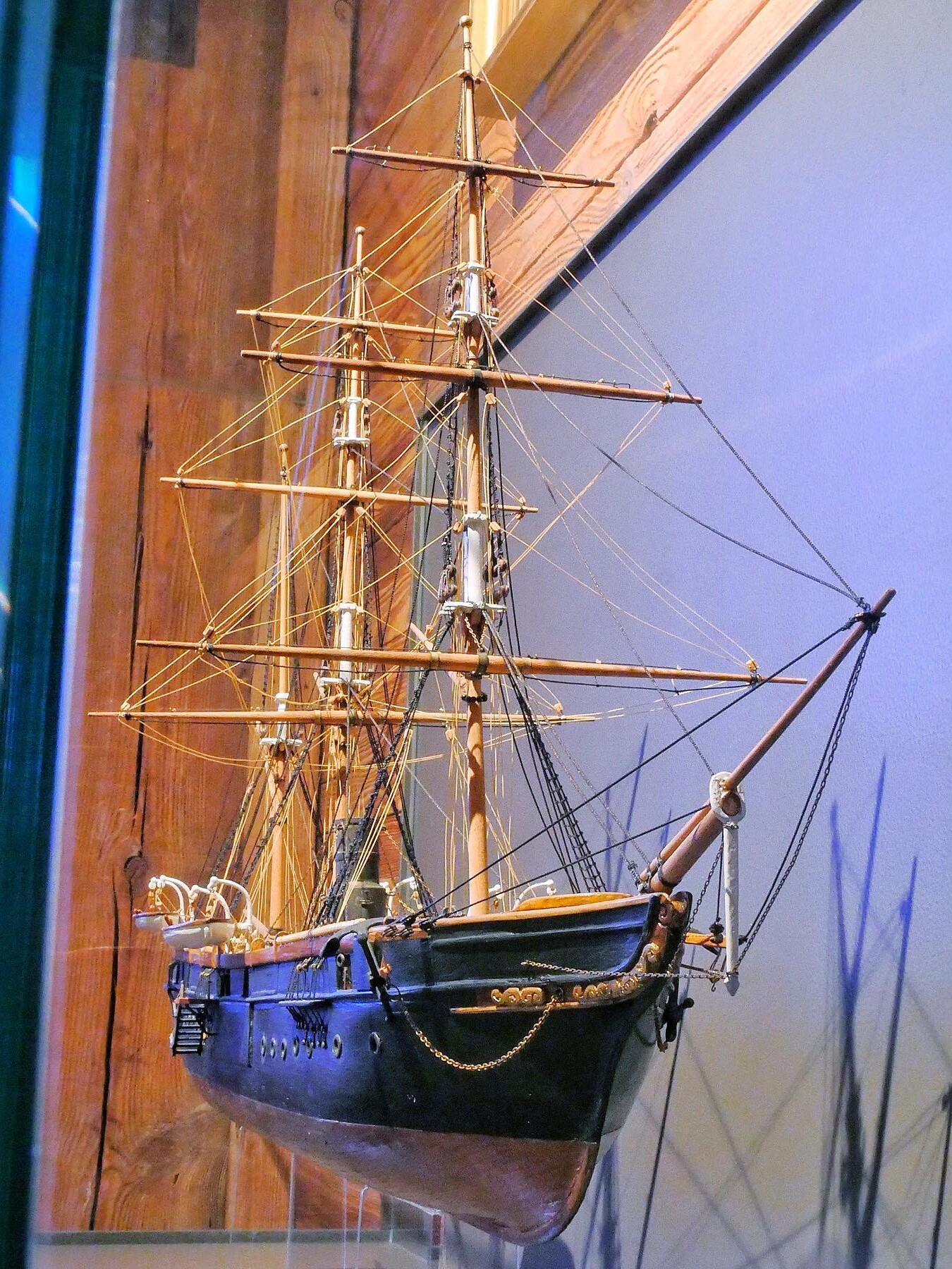 Detailliertes Modell eines historischen Segelschiffs mit mehreren Masten, Takelage und dunkelblauem Rumpf, an Wand montiert.