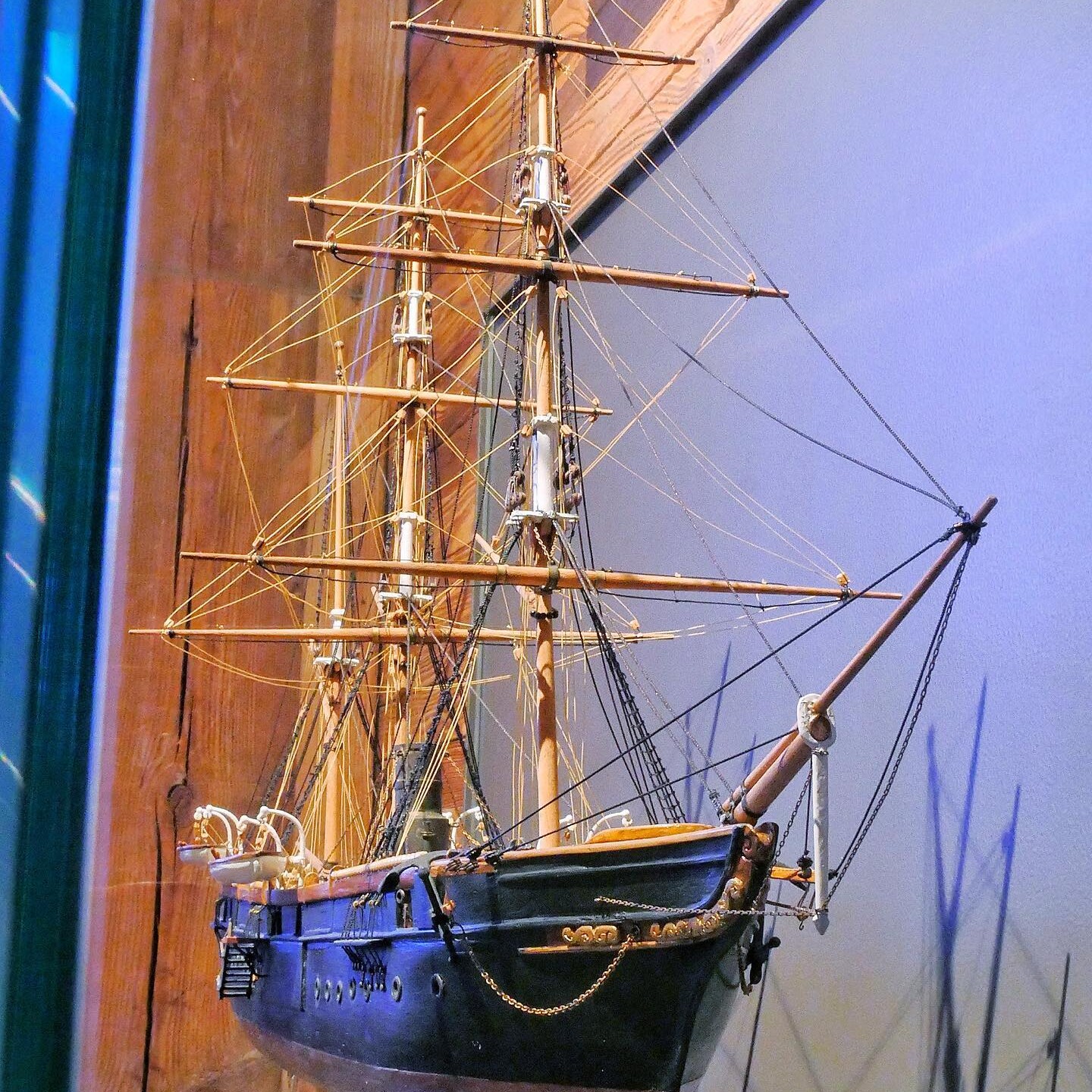Detailliertes Modell eines historischen Segelschiffs mit mehreren Masten, Takelage und dunkelblauem Rumpf, an Wand montiert.