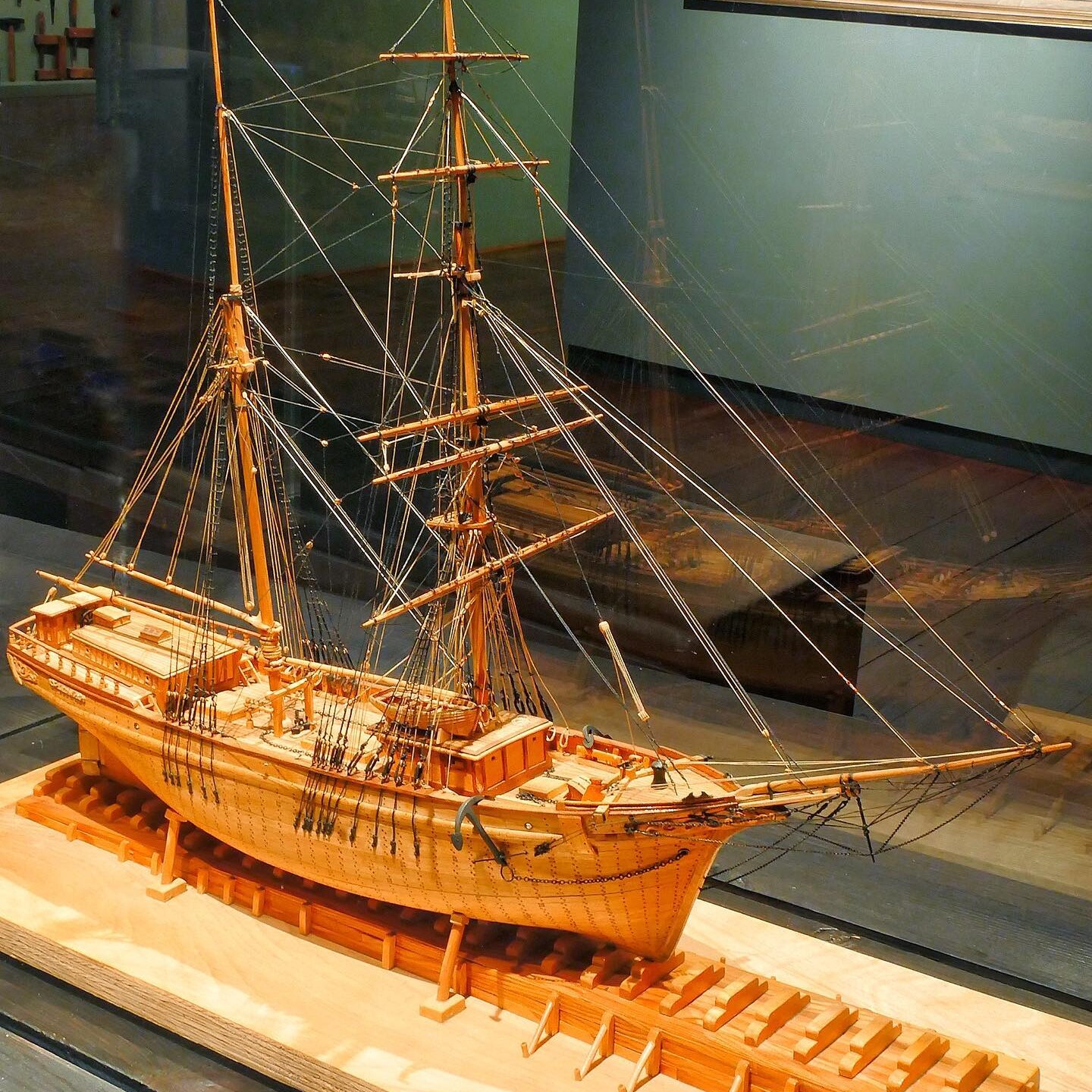 Detailliertes hölzernes Schiffsmodell mit Masten, Takelage und Bugspriet auf Holzgestell in Museumsvitrine.