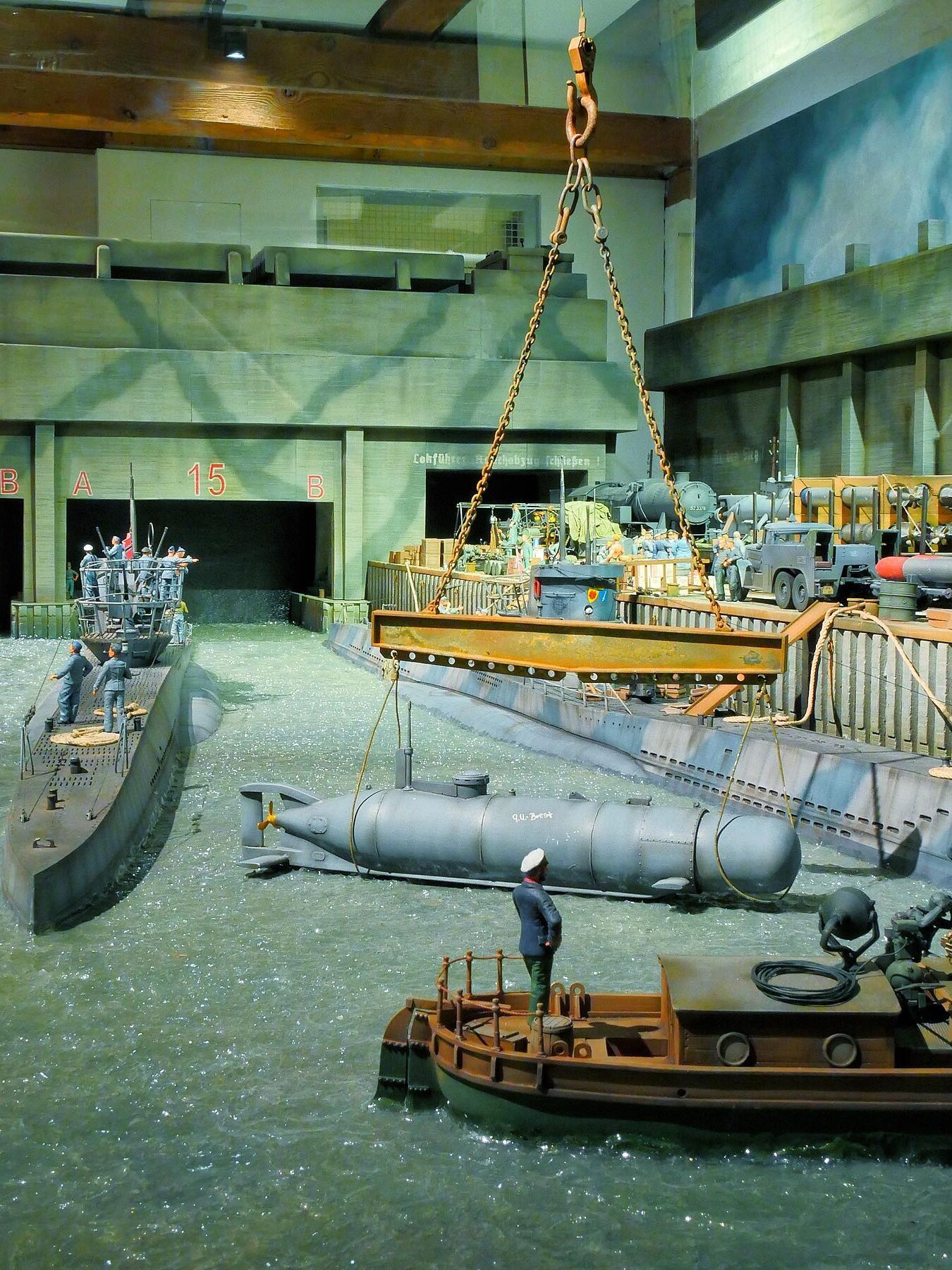 Miniatur-Dockszenerie mit Torpedobooten, Hebekran, einem getakelten Torpedo und Seeleuten an Kais und Pontons.