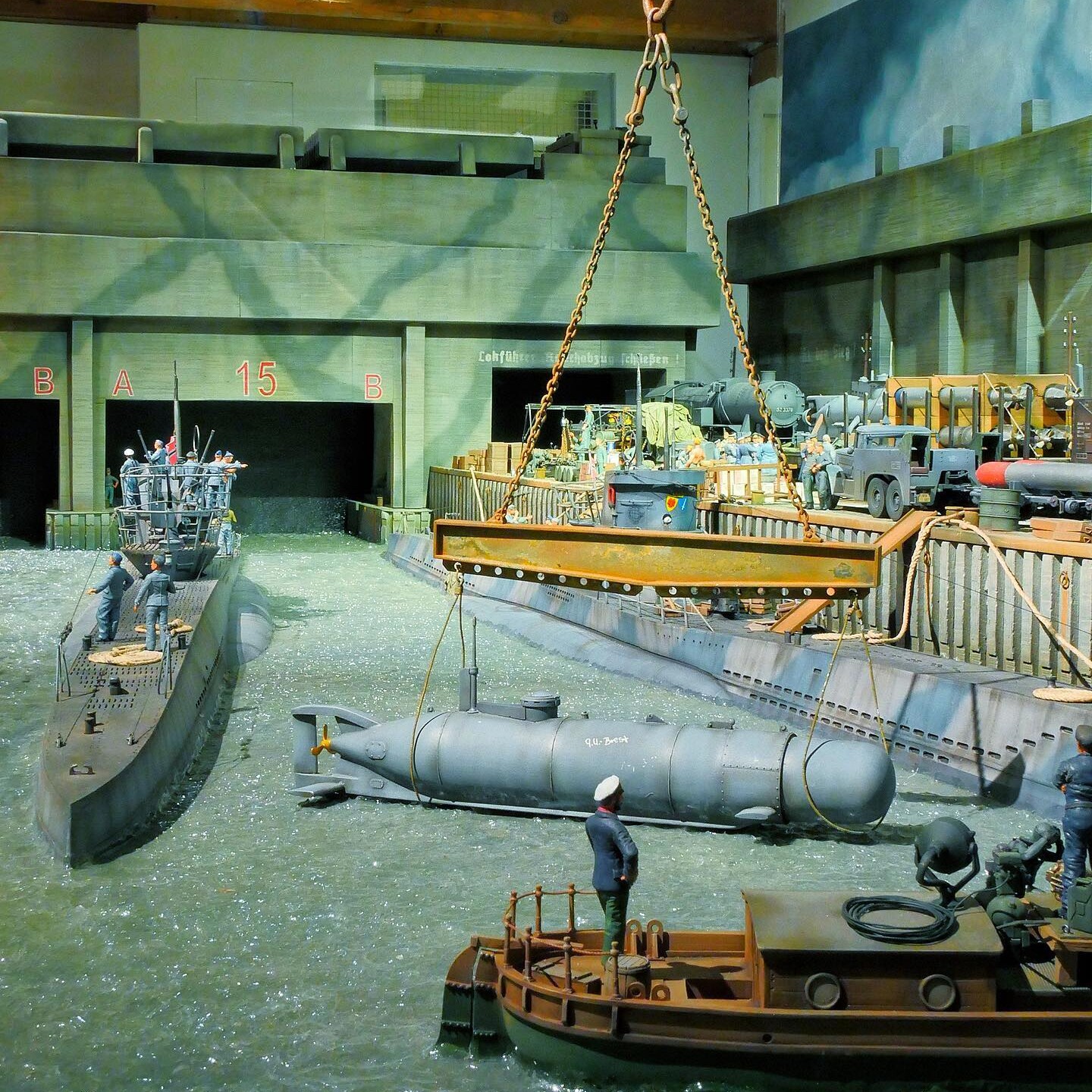 Miniatur-Dockszenerie mit Torpedobooten, Hebekran, einem getakelten Torpedo und Seeleuten an Kais und Pontons.