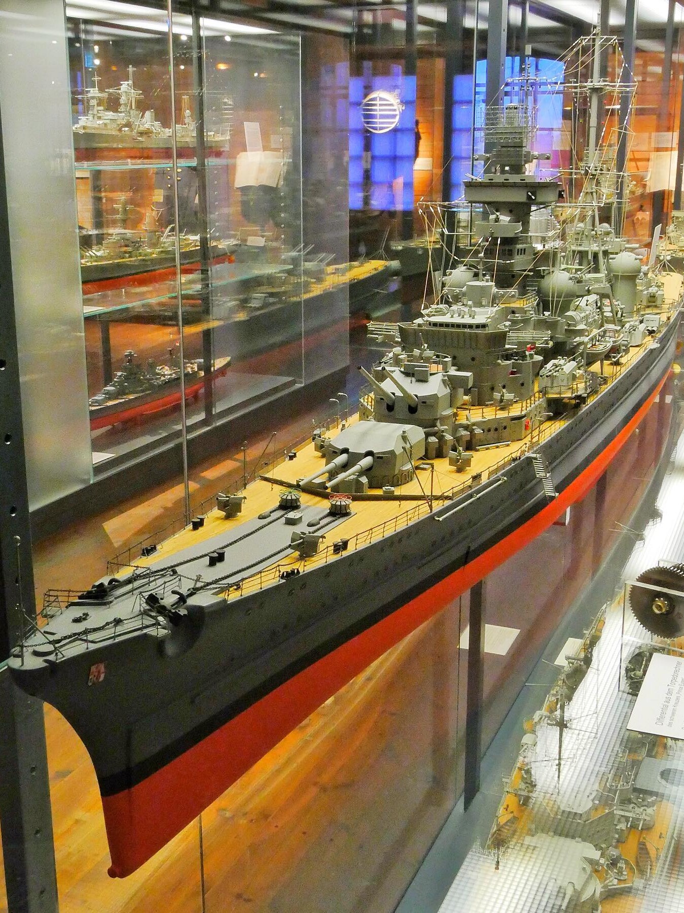maßstabsgetreues Modell eines Kriegsschiffs mit grauem Rumpf, roten Kiellinie und detaillierter Decks‑ und Aufbautenpräsentation in Vitrine