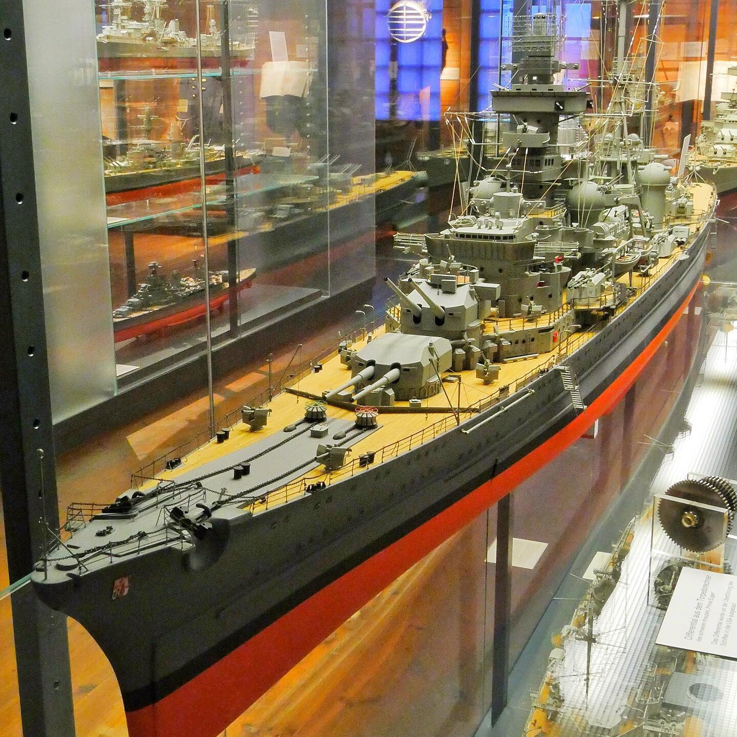 maßstabsgetreues Modell eines Kriegsschiffs mit grauem Rumpf, roten Kiellinie und detaillierter Decks‑ und Aufbautenpräsentation in Vitrine