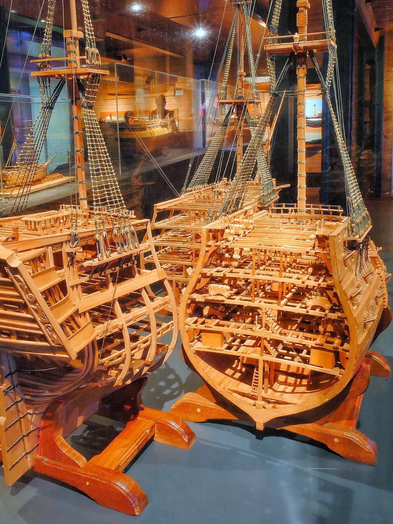 Zwei detaillierte Holzschiffsmodelle mit offener Spantenstruktur, Takelage und Takelnetz in einem Museumsvitrinen-Display.