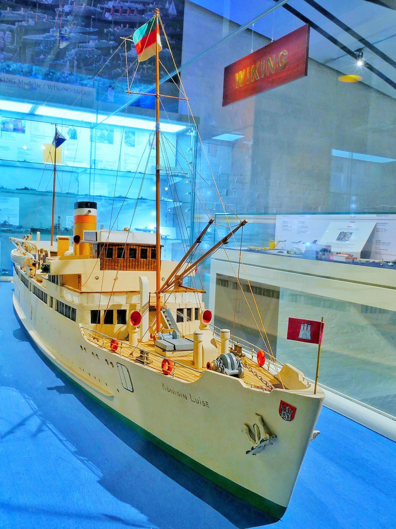 Detailliertes Schiffsmodell namens Königin Luise mit Masten, Flaggen und Rettungsringen in einer Museumsvitrine.