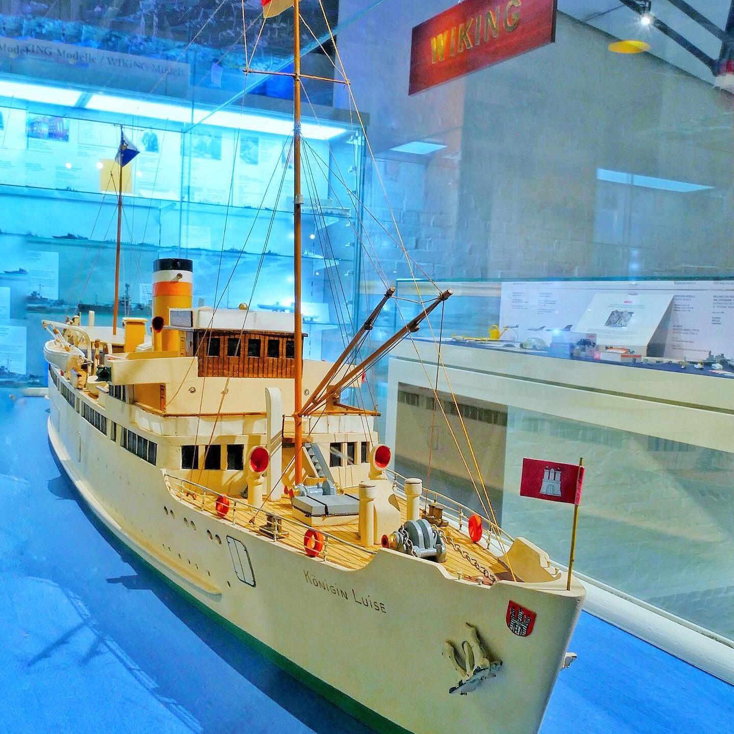 Detailliertes Schiffsmodell namens Königin Luise mit Masten, Flaggen und Rettungsringen in einer Museumsvitrine.