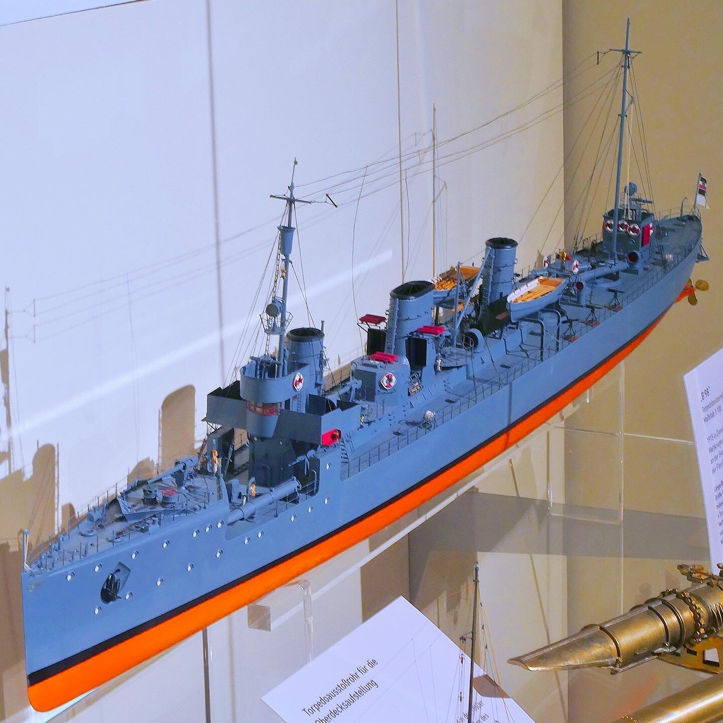 Modell eines graublauen Kriegsschiffs mit zwei Schornsteinen, Masten und feinen Takelage-Drähten, auf Ständern in einer Vitrine ausgestellt