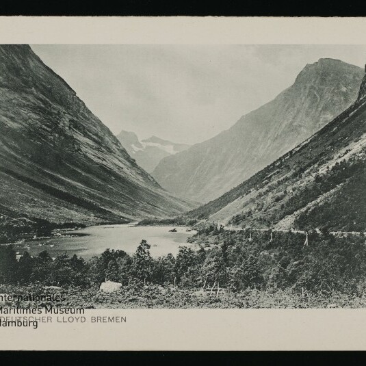 Bergtal mit See und schroffen Hängen, Bäume im Vordergrund und kleiner Schriftzug DEUTSCHER LLOYD BREMEN unten links.