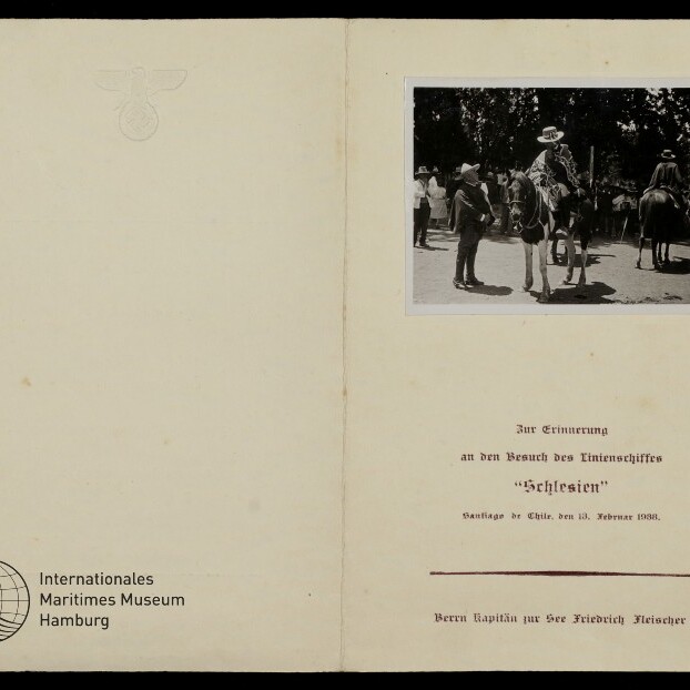 Geöffnetes Erinnerungsheft mit Schwarzweißfoto von berittenen Männern, eingeprägtem Adleremblem oben und deutschem Text.